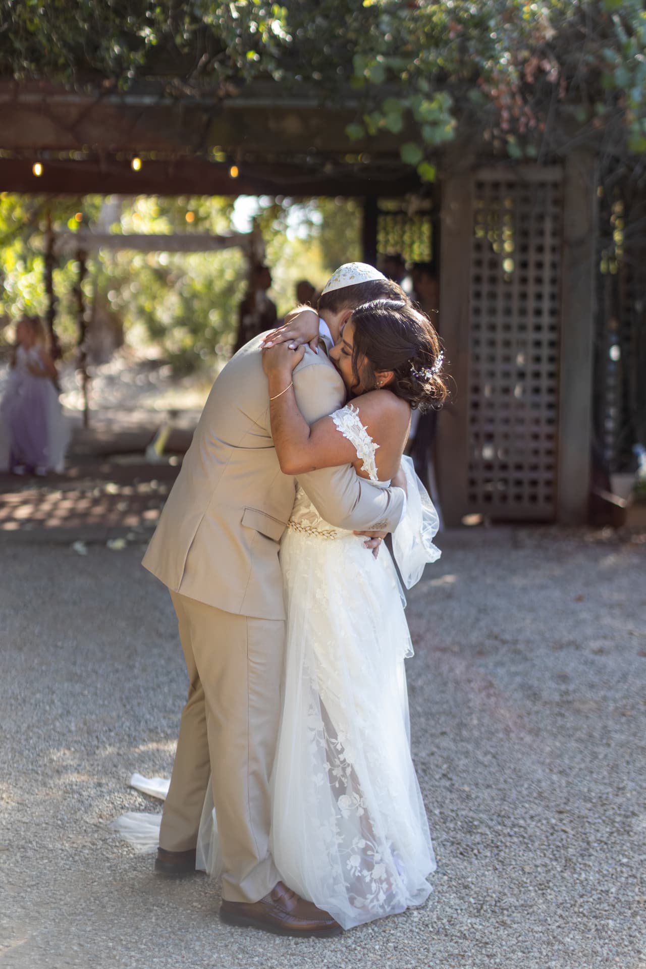 Ashley and Sean sharing an intimate romantic embrace outdoors under a sun-drenched, leaf-covered wooden pergola