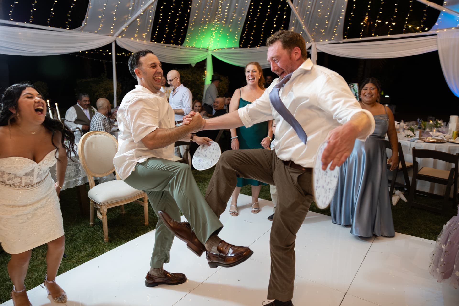 Ashley and Sean celebrating with guests during an exuberant night of dancing on a white dance floor under a brightly lit reception tent