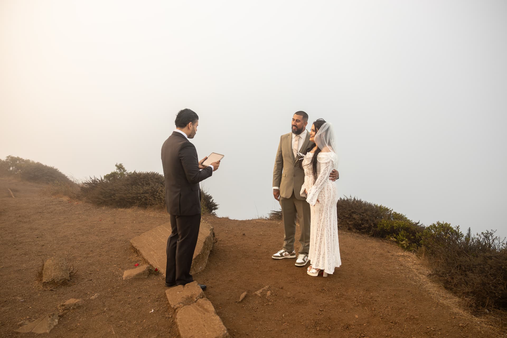 Officiant reading from a tablet as the bride and groom stand together during their ceremony on a foggy cliffside, Crystal & Joey wedding