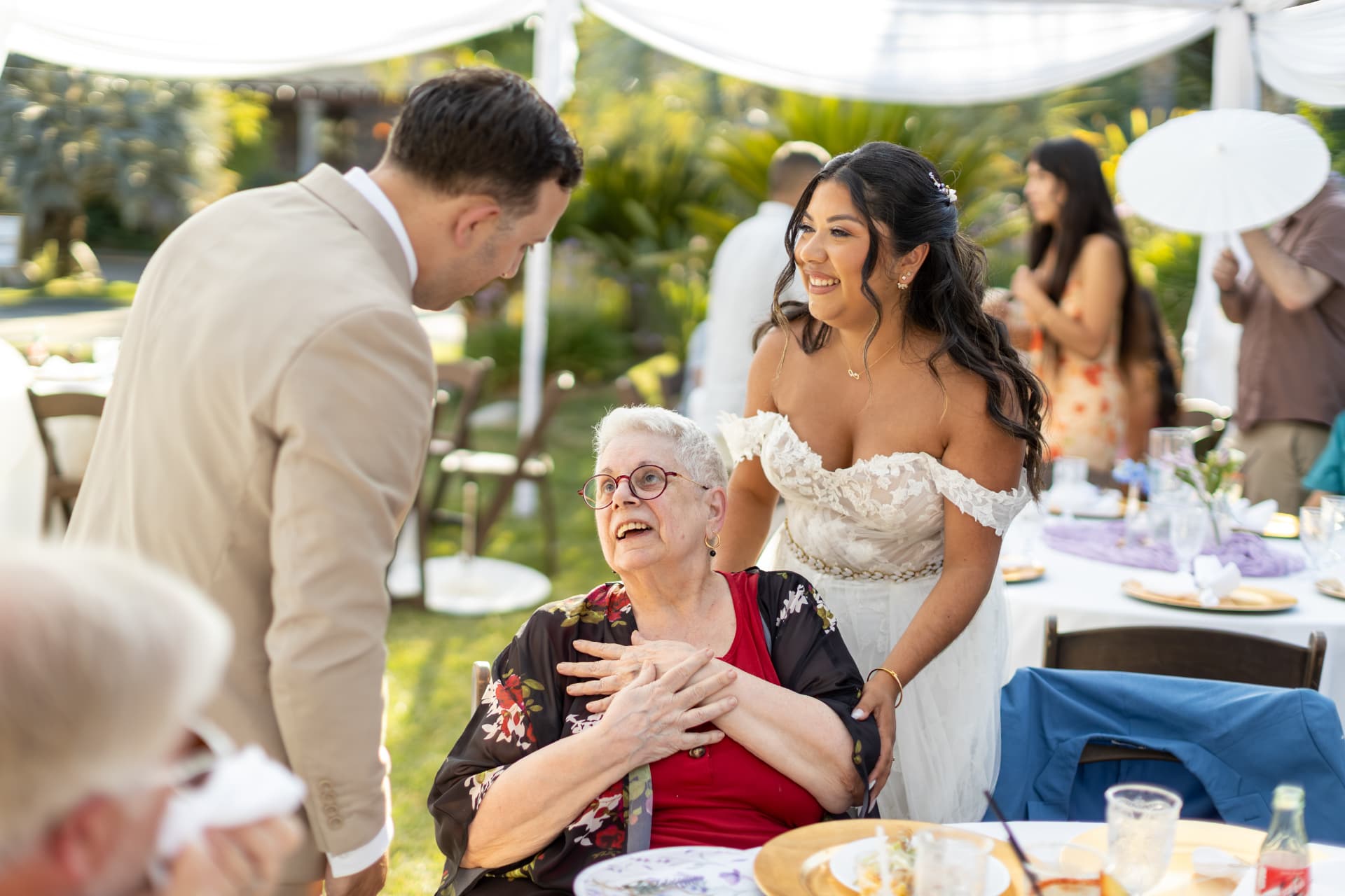Bride leaning in to share a tender moment with a seated elderly woman at the reception while the groom stands nearby, Ashley & Sean wedding