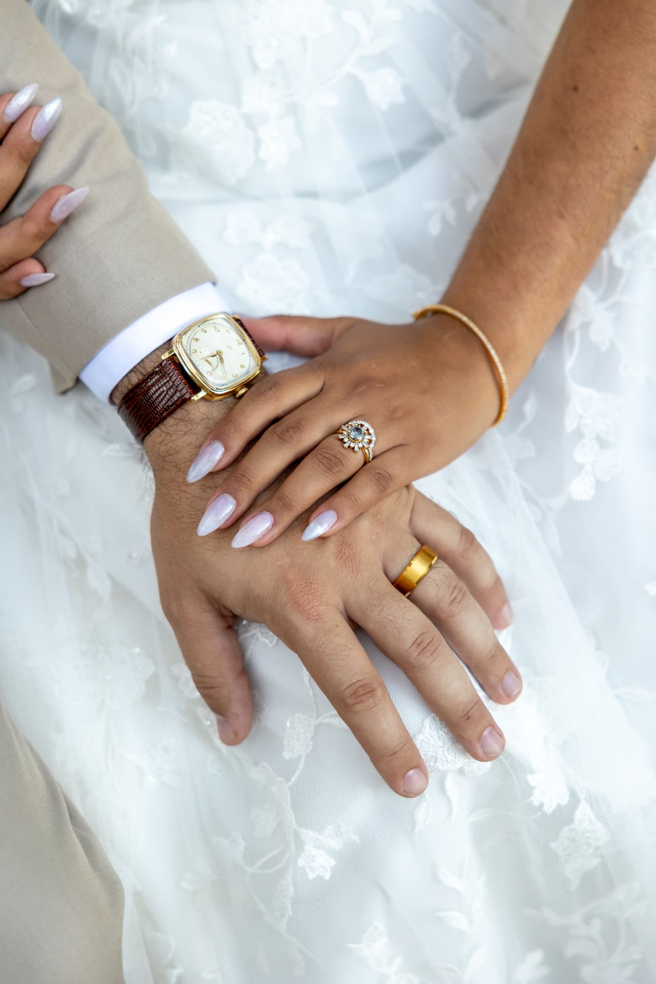 Close-up of the bride and groom's hands showing their wedding rings over her lace dress