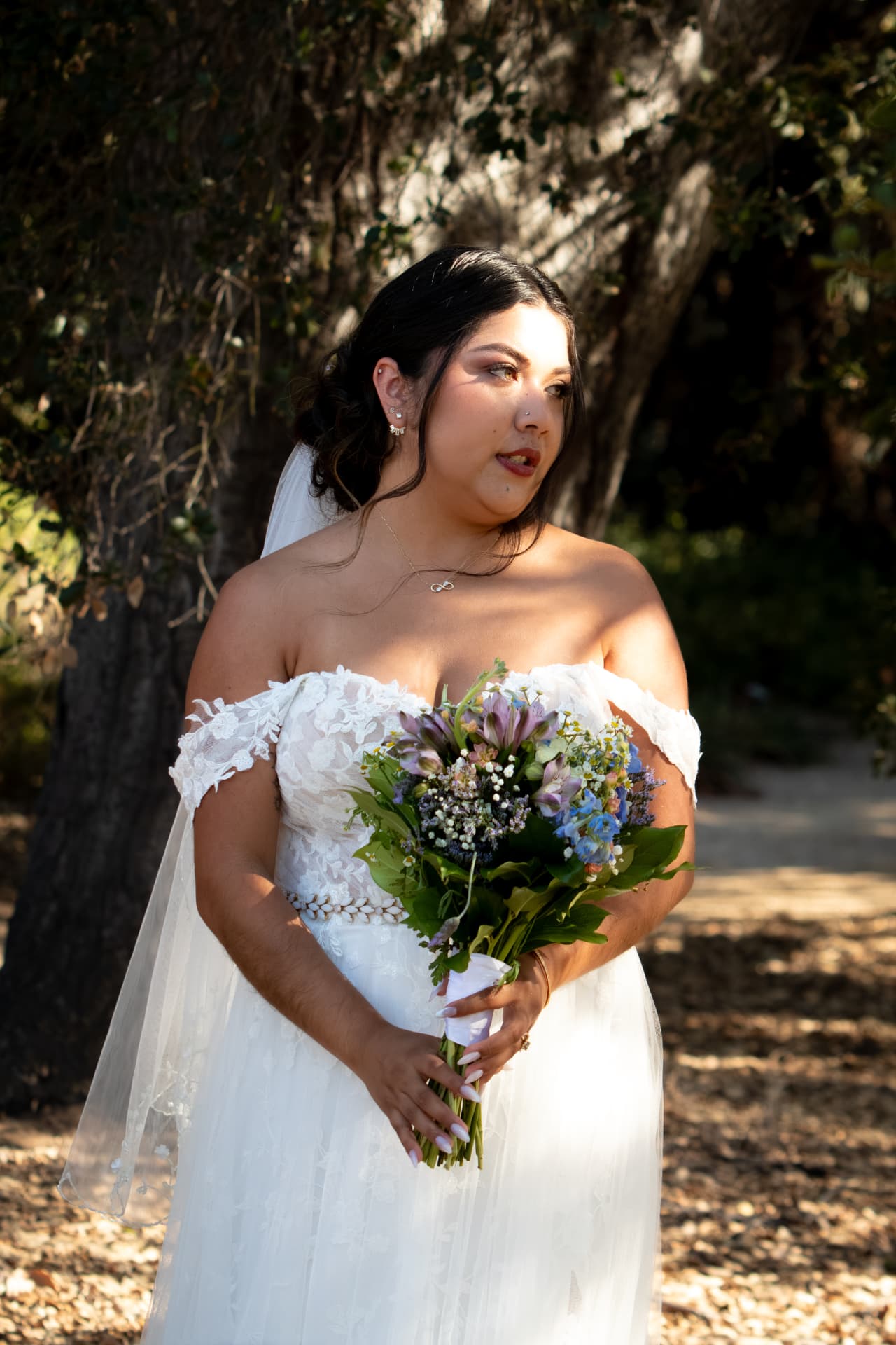 Bride holding her bouquet in dappled light beneath the trees