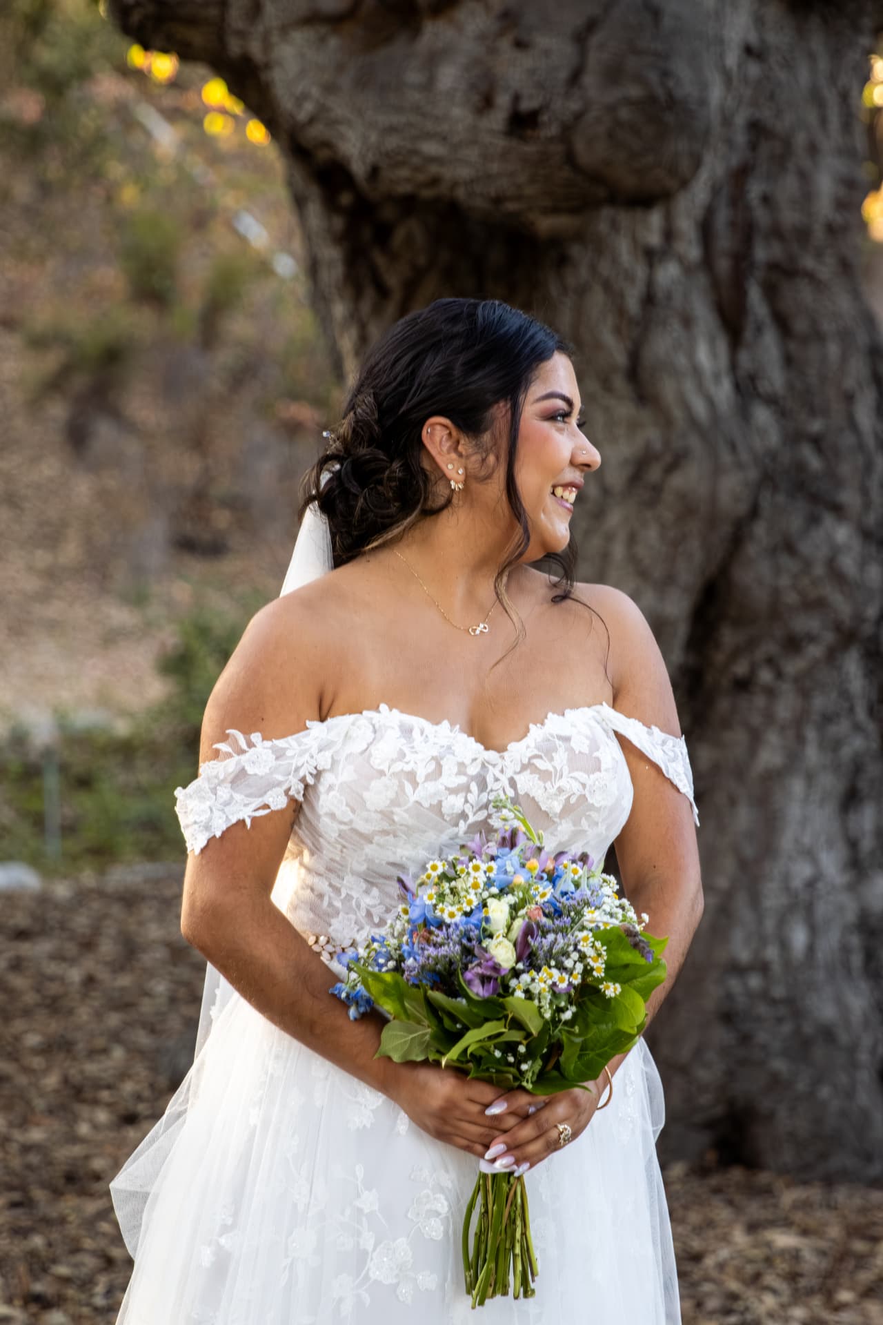 Bride laughing while holding her bouquet in front of a large oak tree