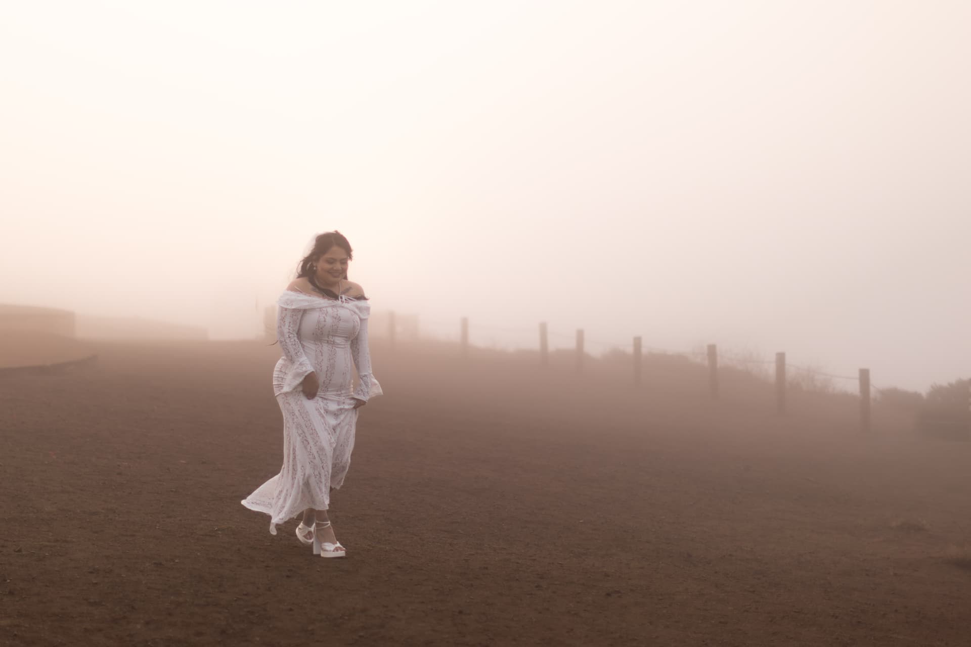 Bride in a white lace dress walking across a dirt landscape shrouded in warm fog, Crystal & Joey wedding