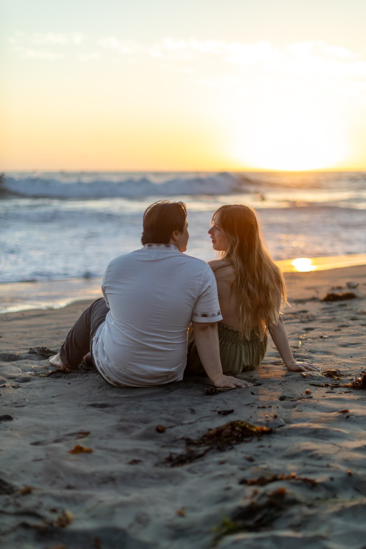 Couple sitting on the beach facing each other at sunset, the sun glowing over the ocean, Anna & Brian couples session