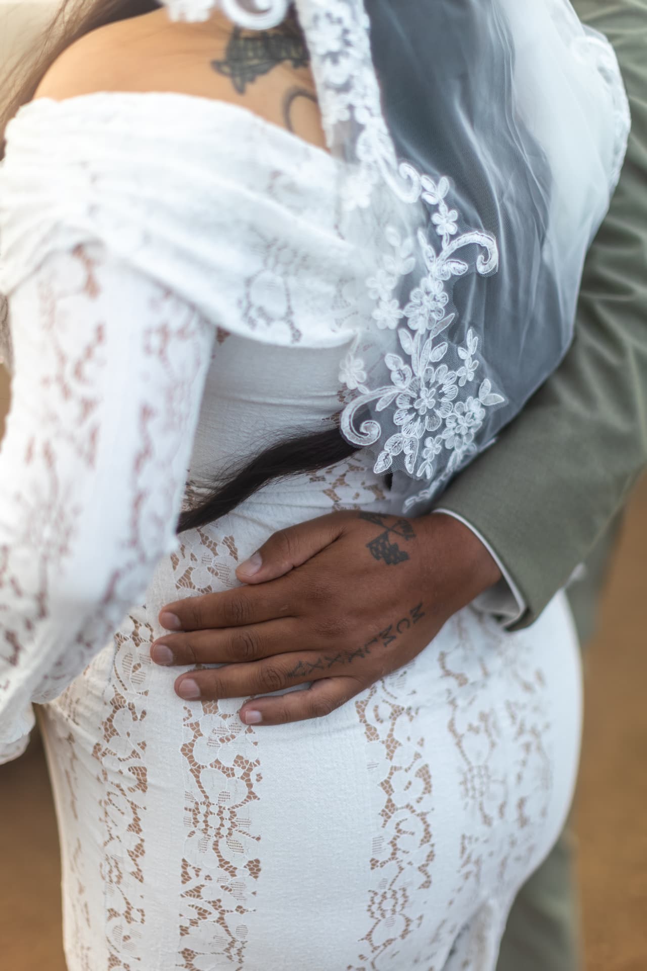 Intimate close-up of the groom's tattooed hand resting on his bride's lace-covered waist, both in long sleeves, Crystal & Joey wedding