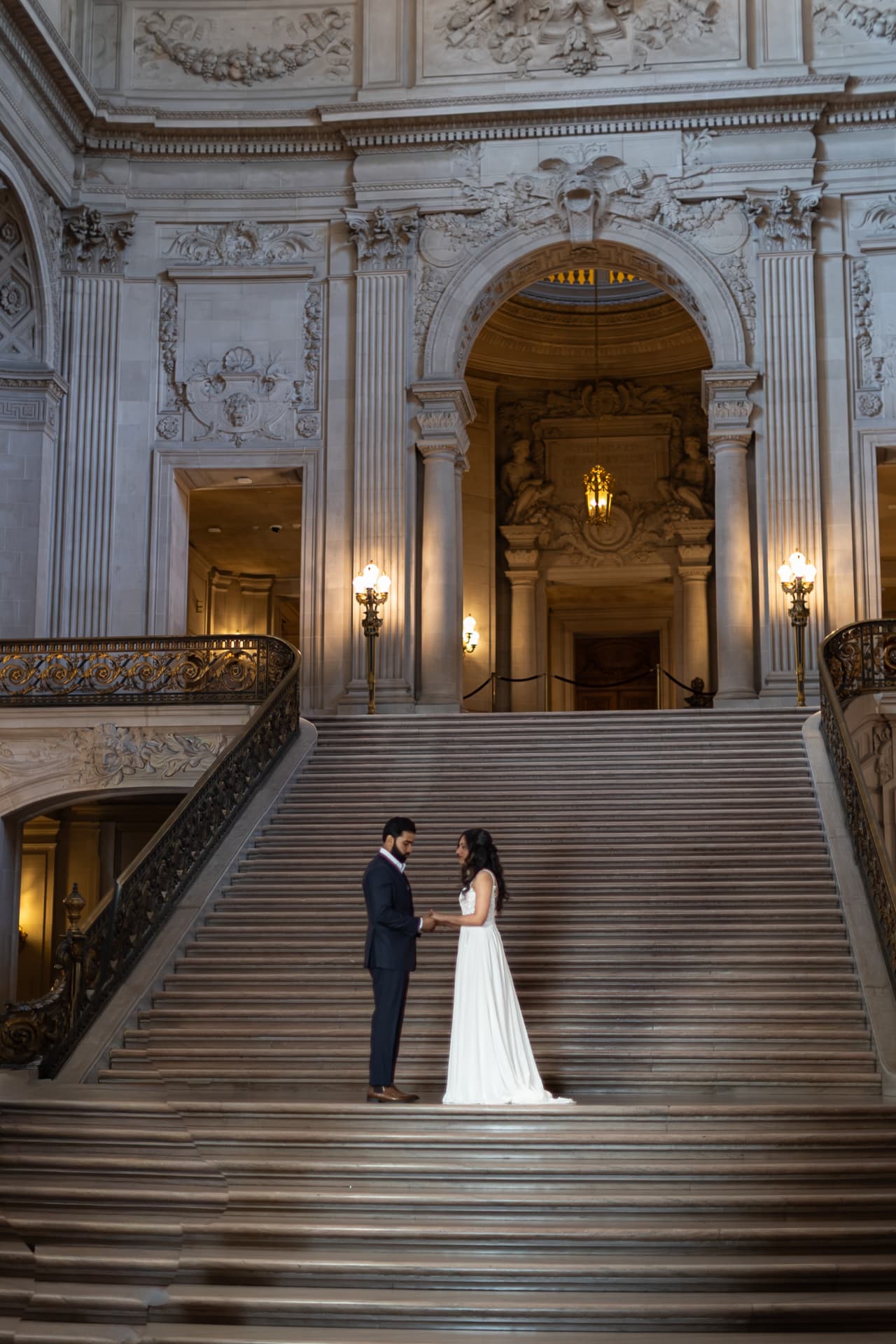 Bride and groom facing one another on a sweeping marble staircase