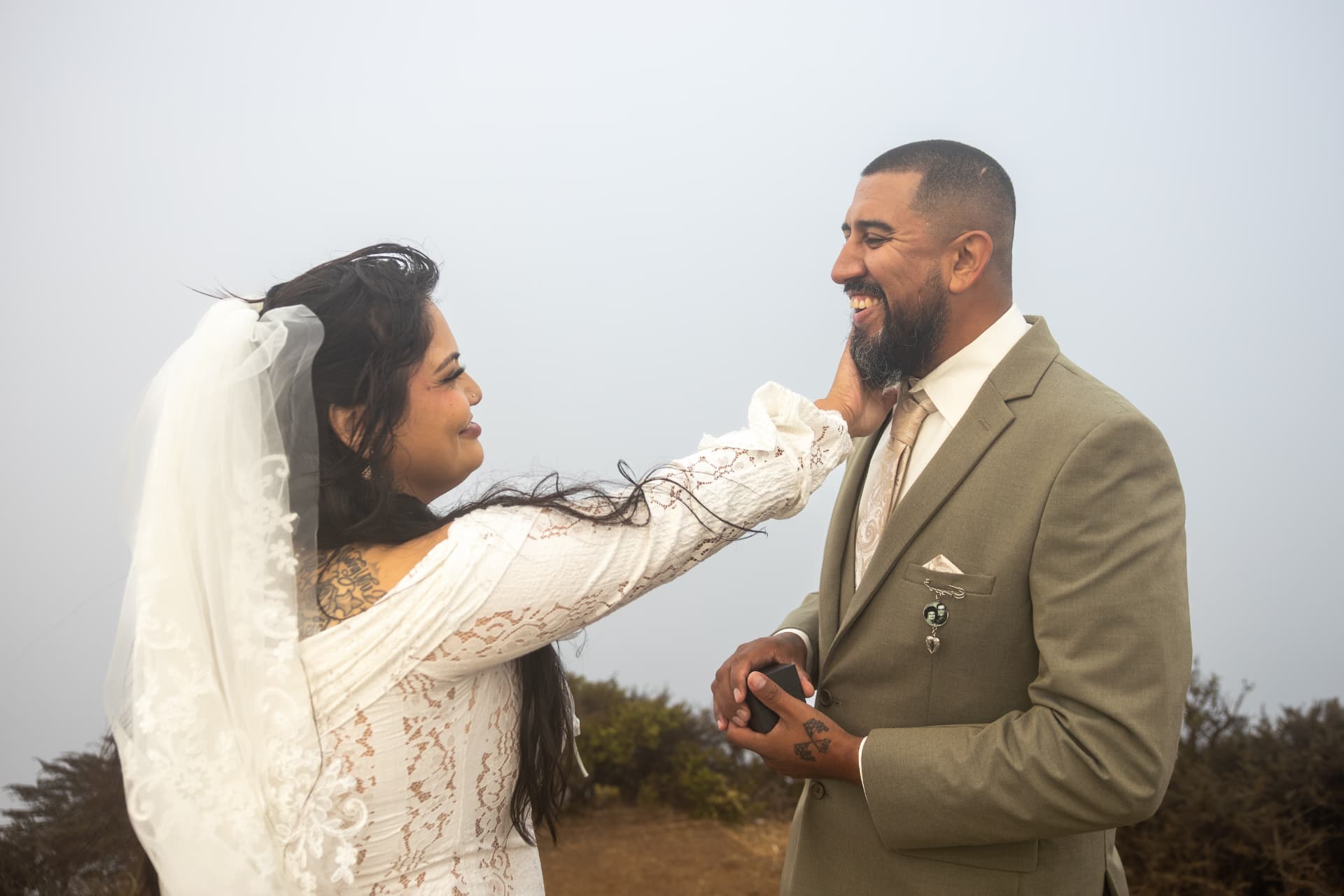 Bride tenderly touching the groom's face as they share a joyful moment under a misty white sky, Crystal & Joey wedding